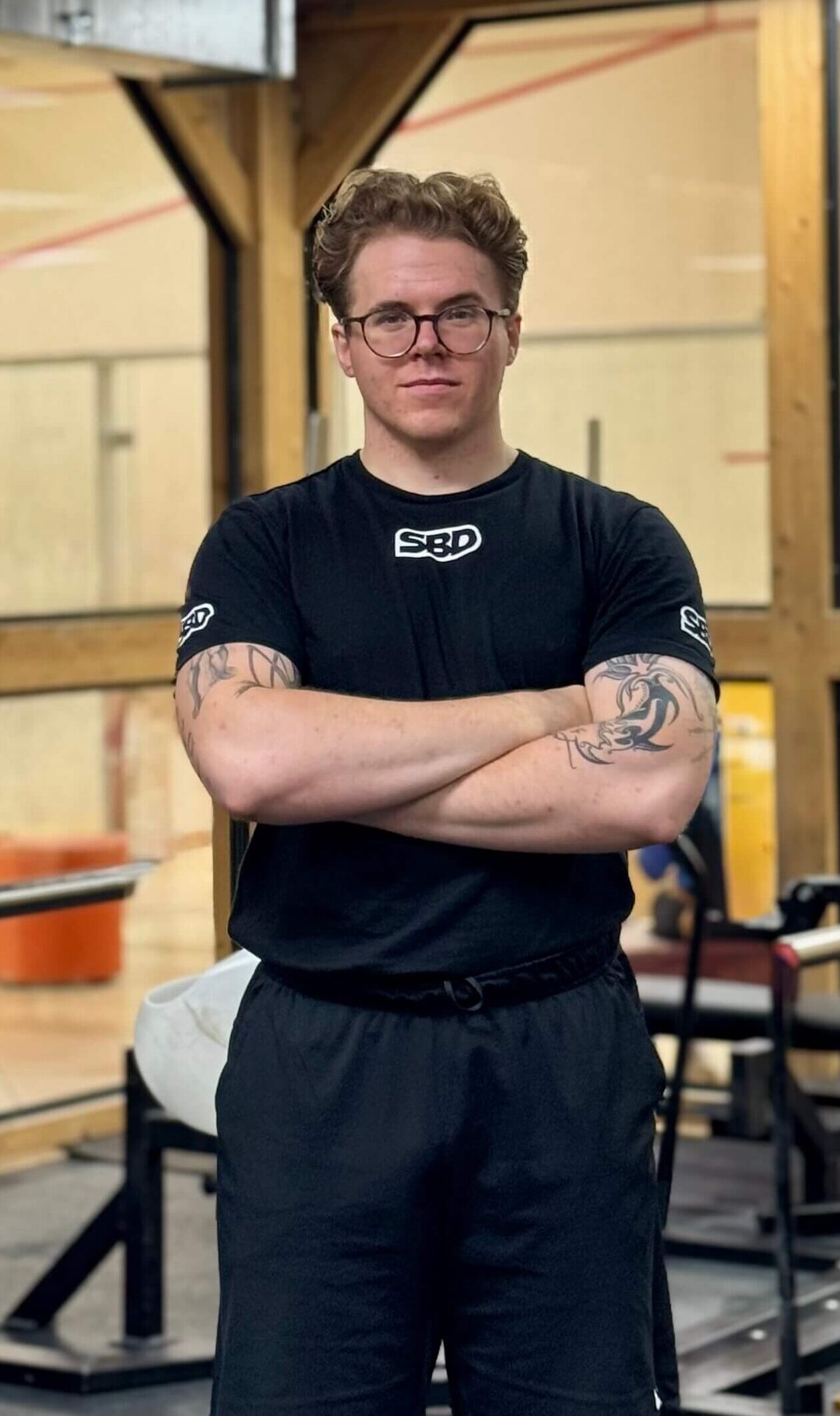 Trener personalny w czarnej koszulce na tle siłowni